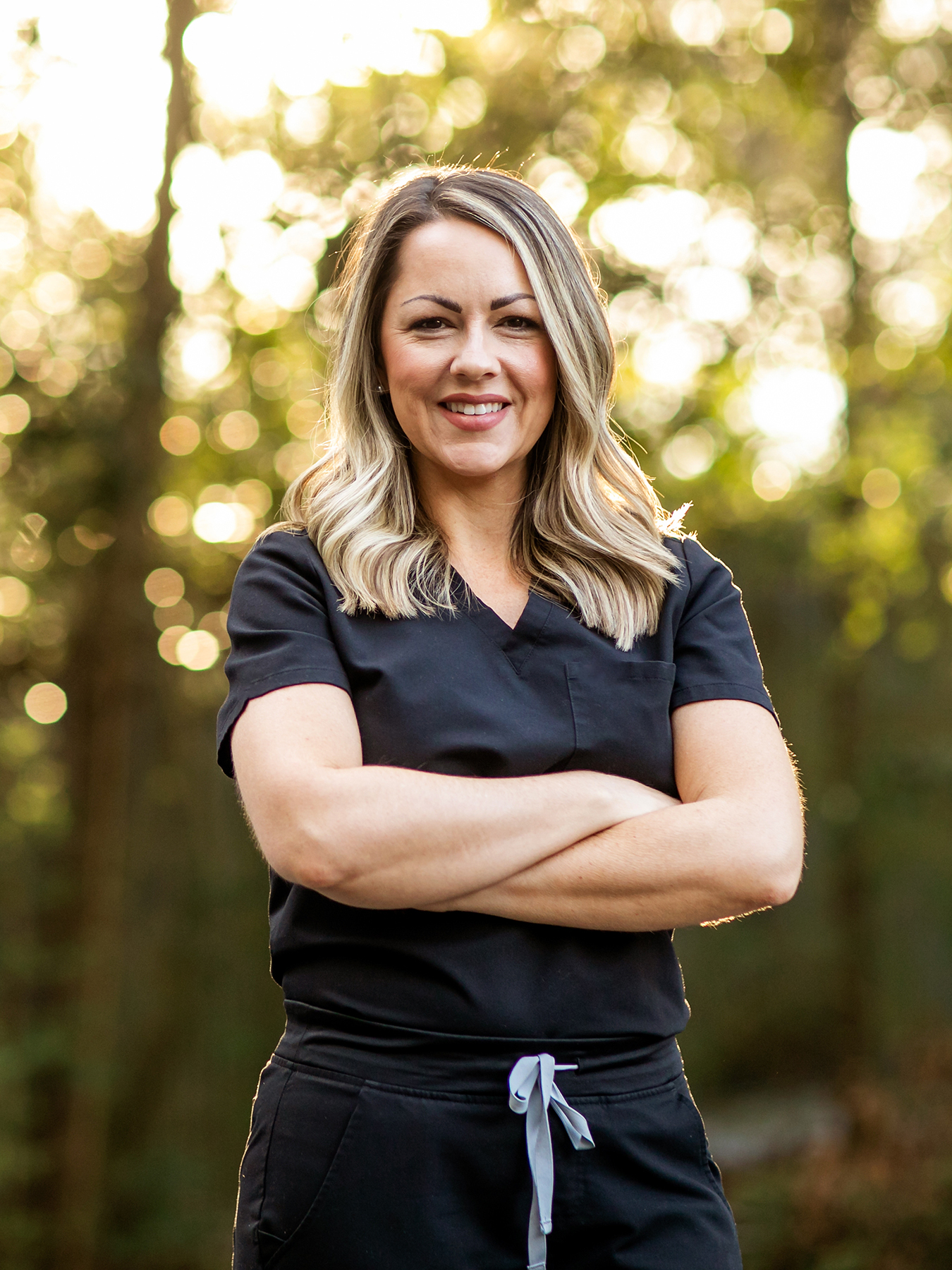 Image of a medical professional with black scrubs and her arms crossed with long hair outside in a natural background with copy space.