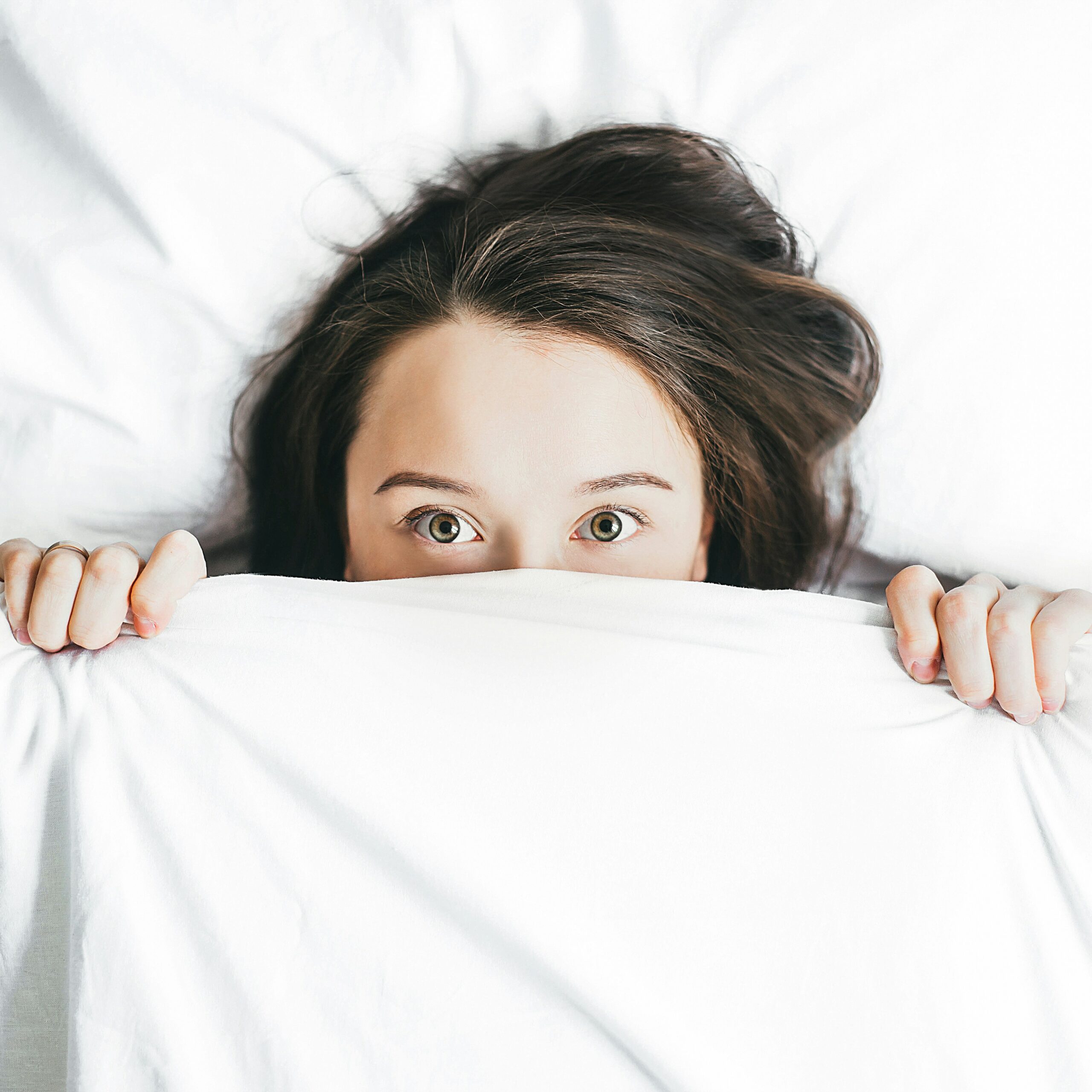 Woman peeping above covers in bed